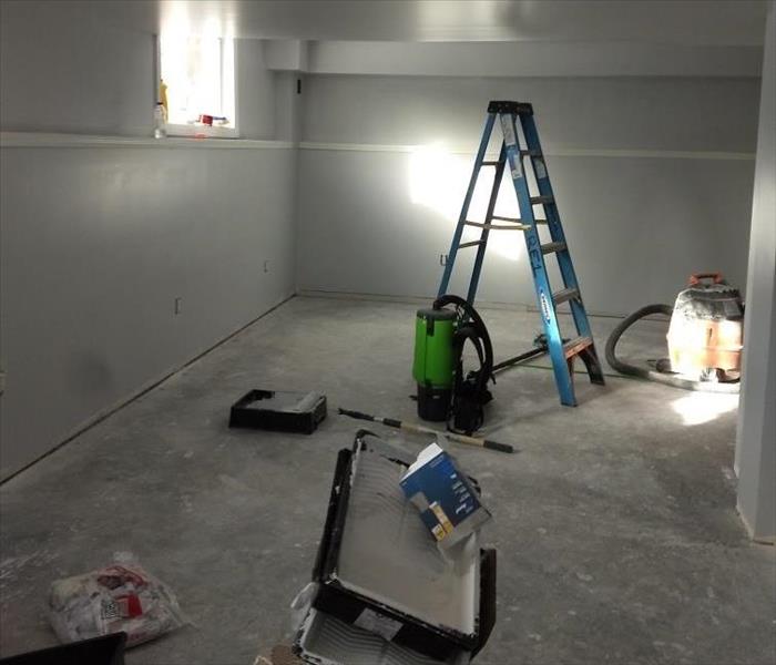 A view of a corner of a damaged basement, floors removed, with a ladder and SERVPRO drying and cleaning equipment throughout